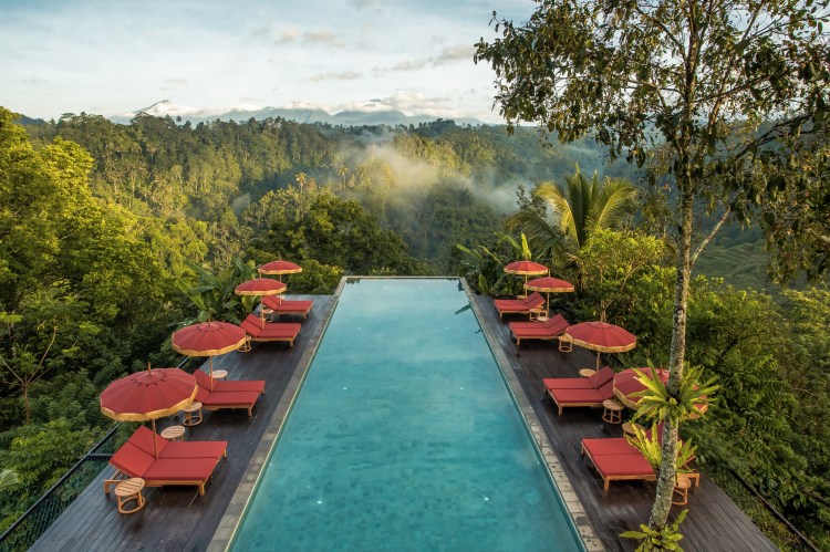A scenic view of Bali's tropical beach at sunset with palm trees, turquoise waters, and tourists relaxing ideal for Bali holidays 2025